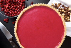 cranberries in a bowl next to a large tart with red filling and spices